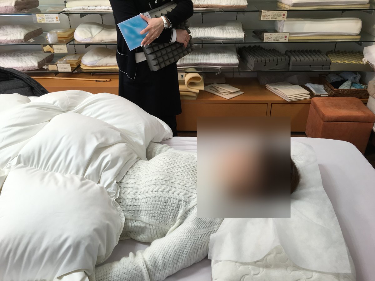 寝具店で、作った枕を敷いたマットレスに仰向けで寝て、高さを確かめているところ